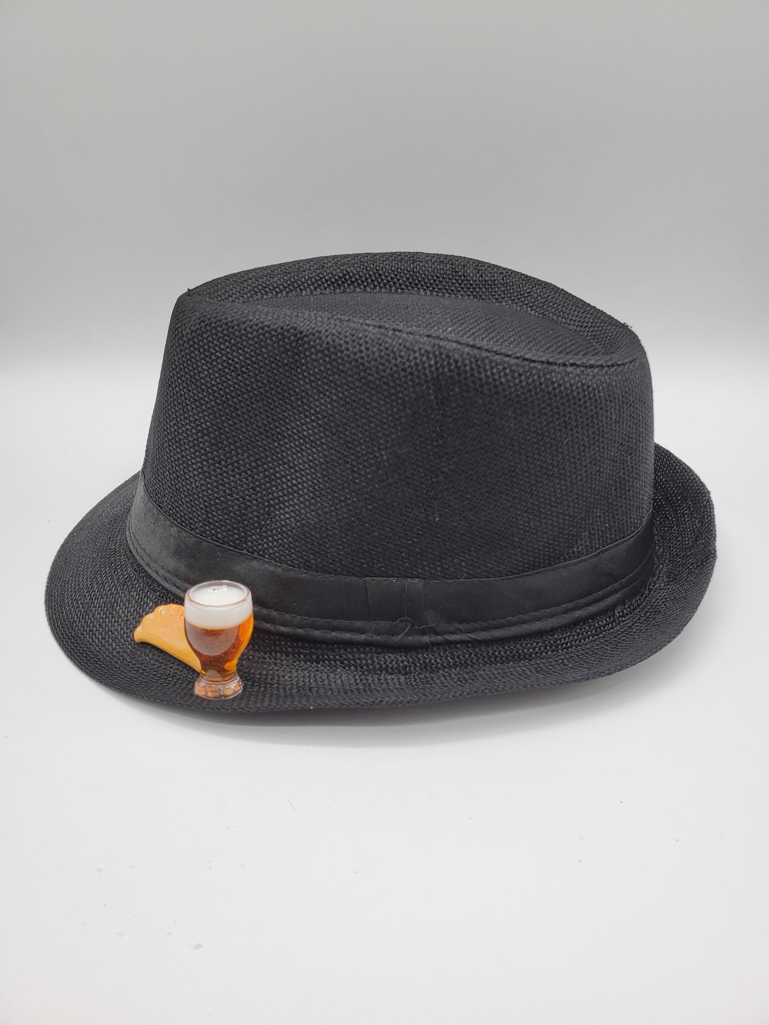 Black fedora Pierogi hat with a textured weave and a decorative pin featuring a glass of beer and a pierogi
