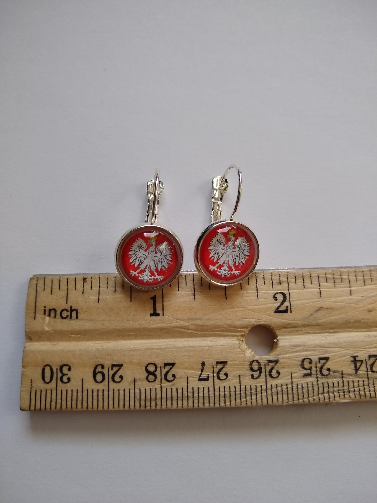 Lever back earrings with Polish Eagle with Crown with a silver colored (not real silver) base next to a ruler showing measurement.